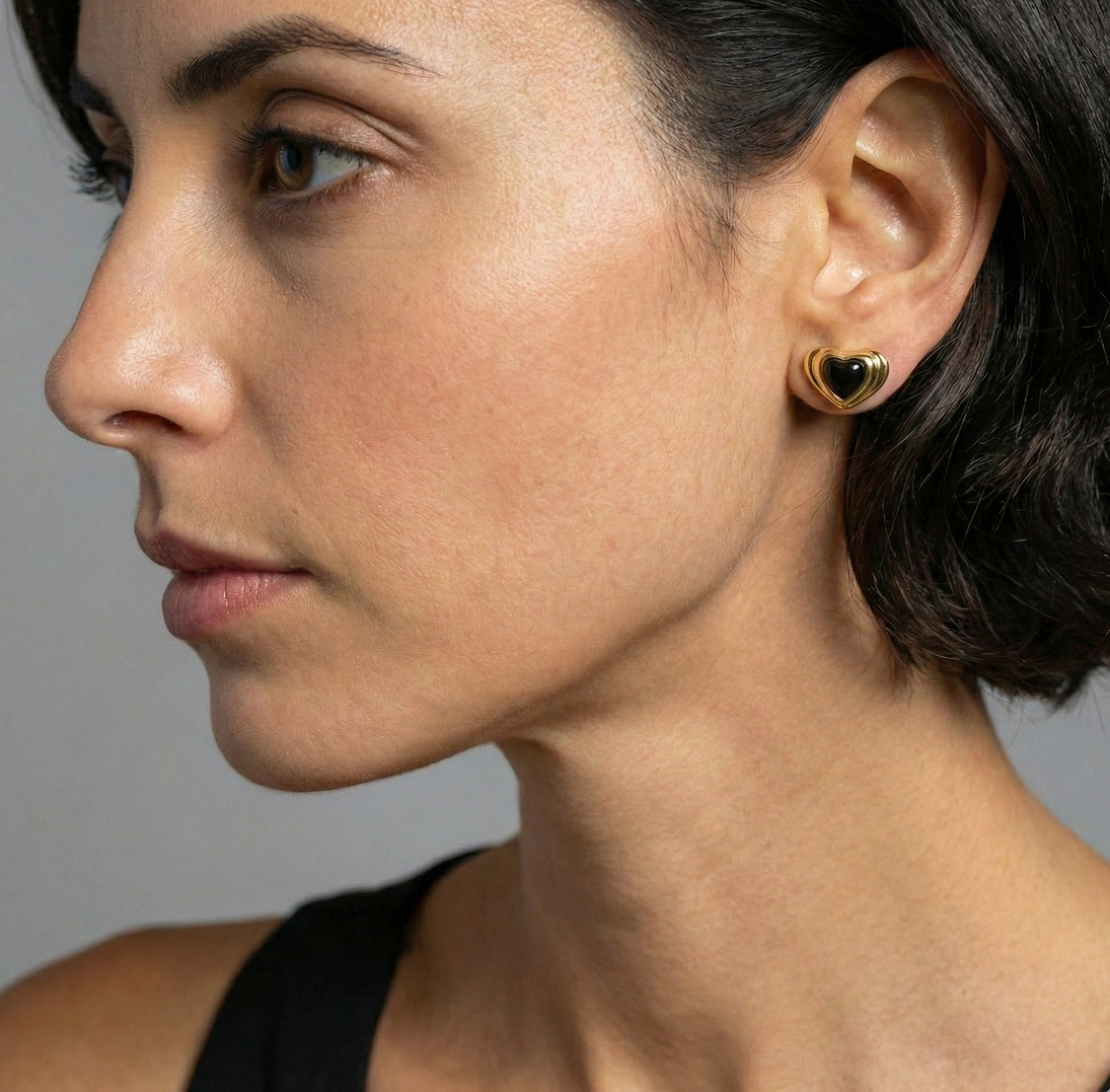 Close-up of a woman wearing a gold heart-shaped earring against a neutral background