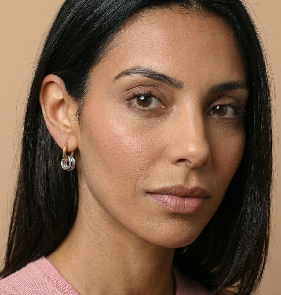 Close-up of a woman with dark hair and earrings against a beige background
