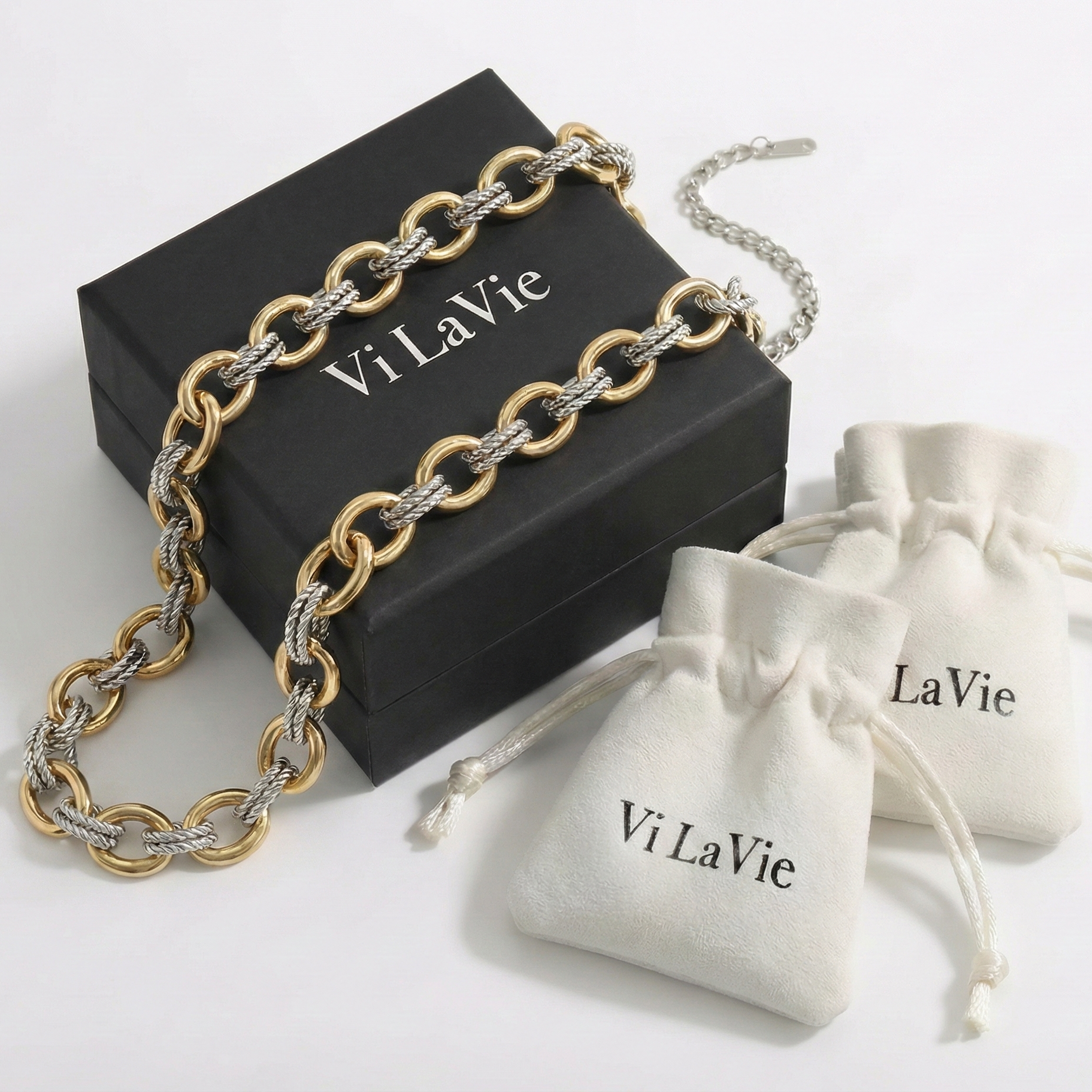 Gold and silver chain necklace on a black 'Vi La Vie' box with two white drawstring bags.