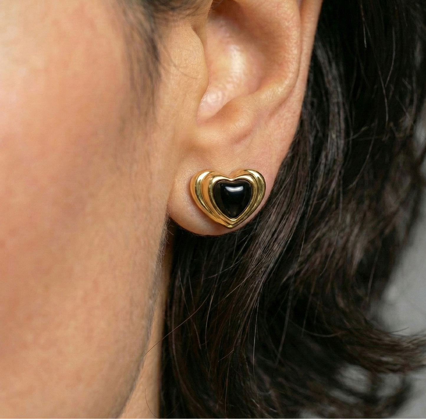 Gold heart-shaped earring with black center worn by a person.