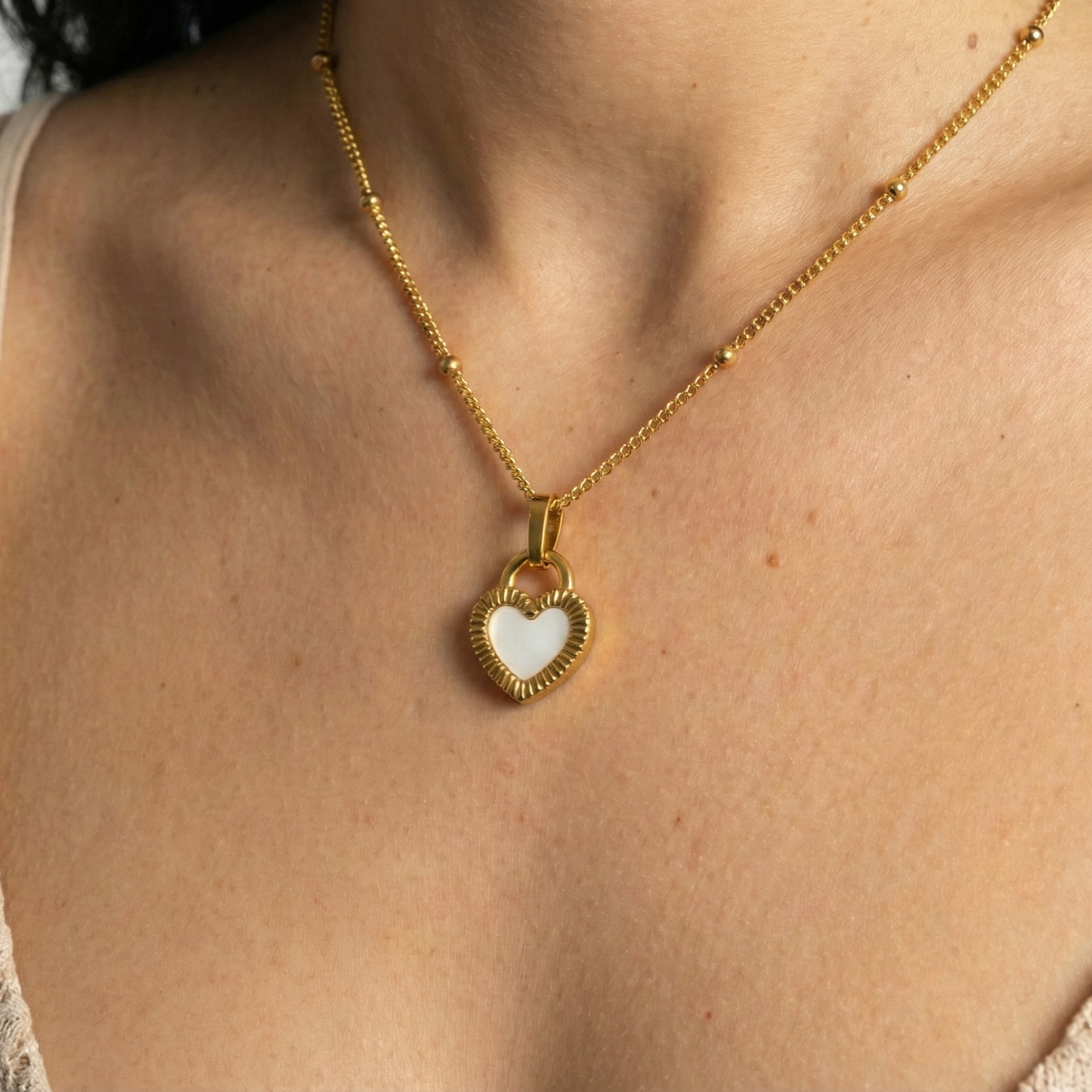 Gold necklace with a heart-shaped pendant on a person wearing a beige top.