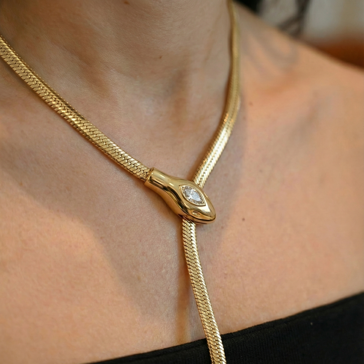 Gold snake necklace with a diamond on a person's neck