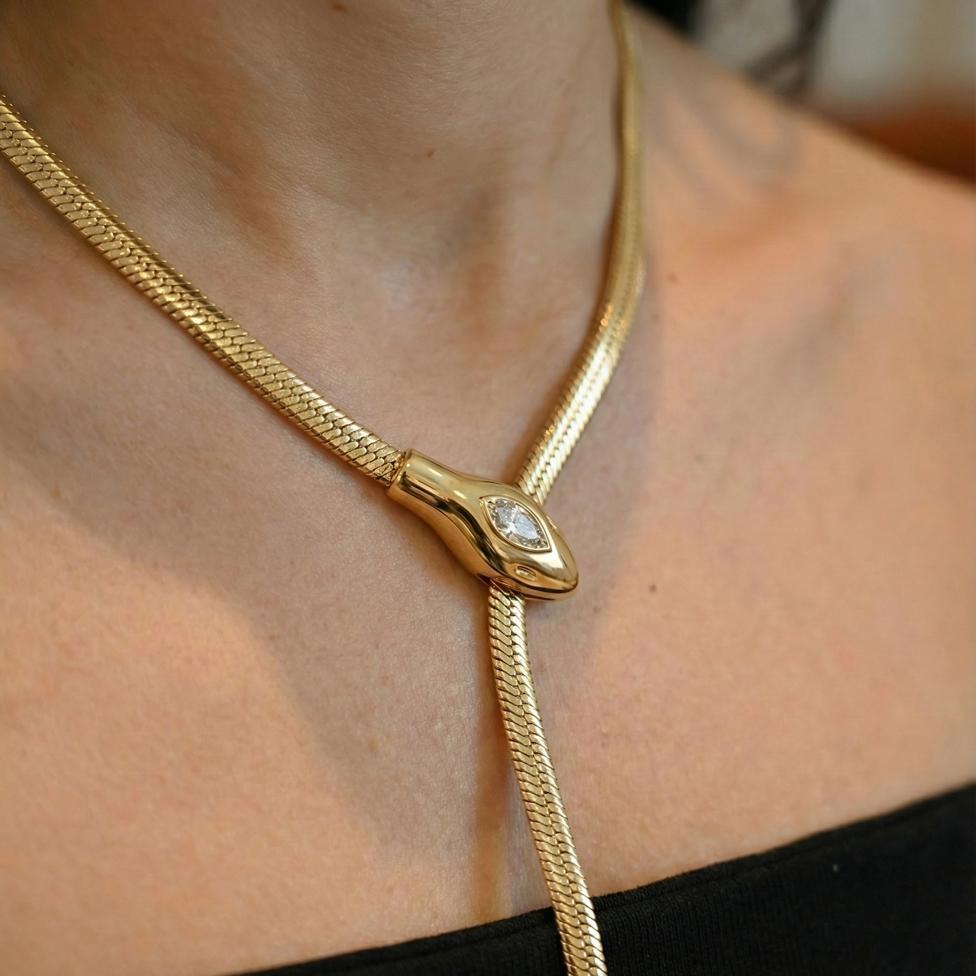 Gold snake necklace with a diamond on a person's neck