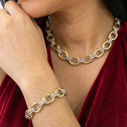 Person wearing a gold and silver chain necklace and bracelet on a red garment.