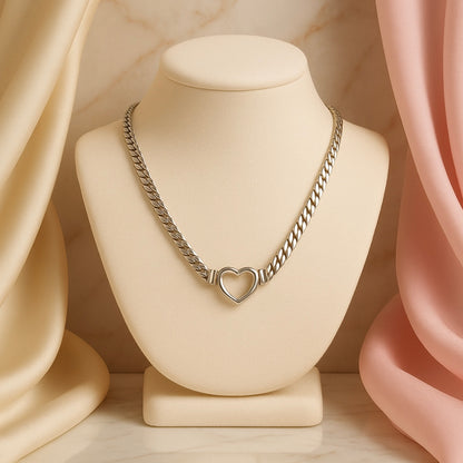 Silver chain necklace with a heart pendant on a beige mannequin bust against a soft pink and beige background.