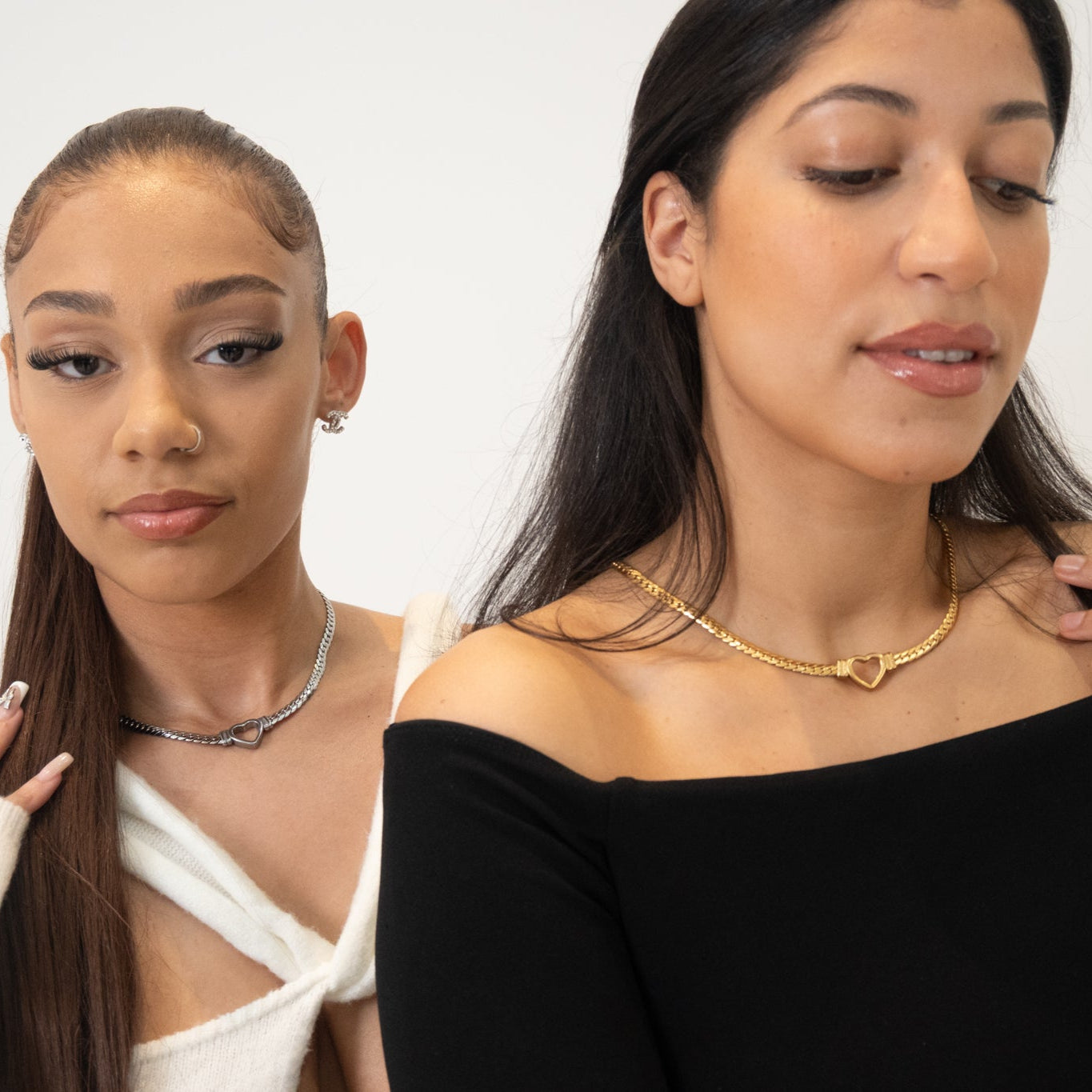 Two women wearing necklaces against a plain background