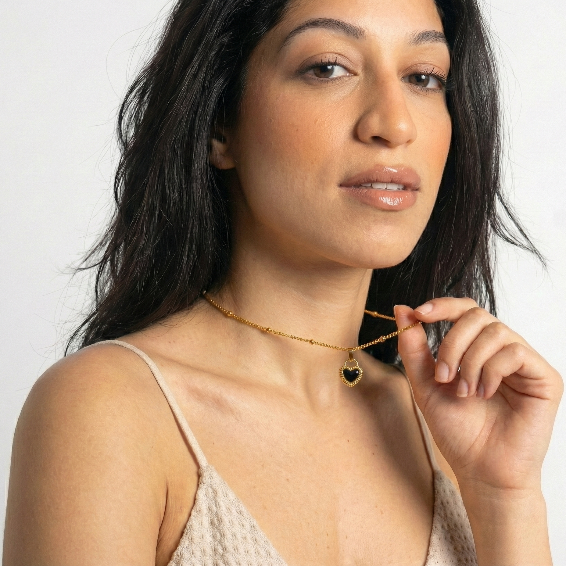 Woman wearing a gold necklace with a heart pendant against a white background