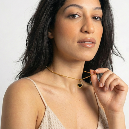 Woman wearing a gold necklace with a heart pendant against a white background
