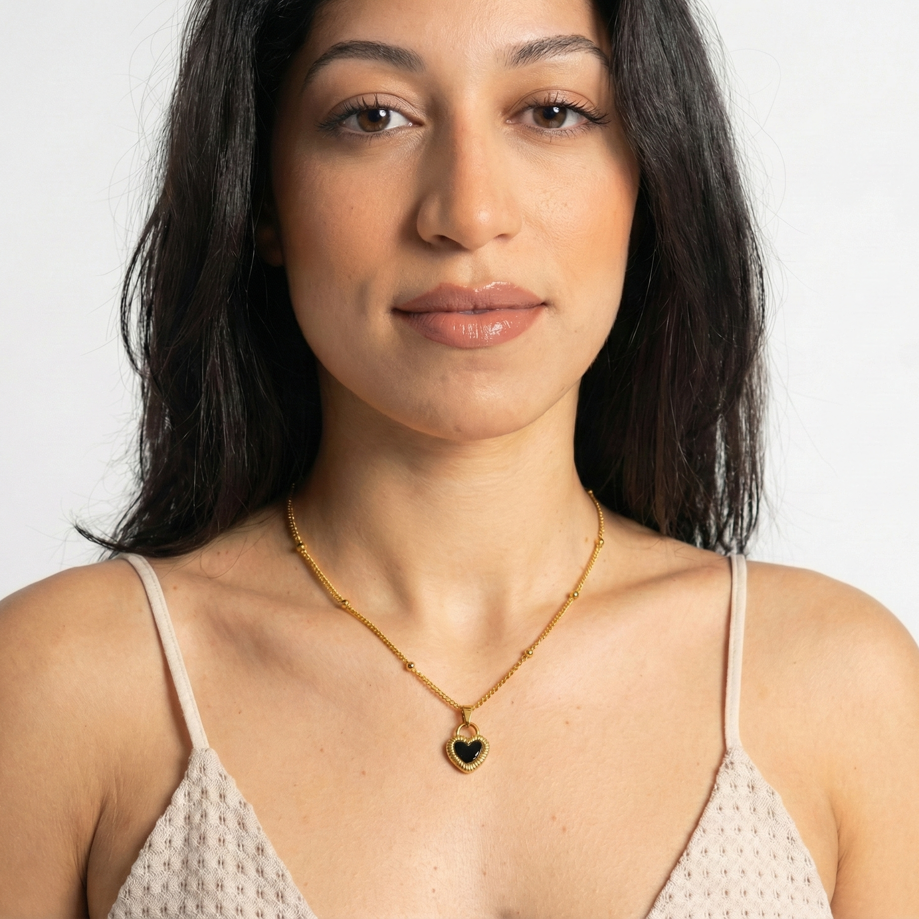 Woman wearing a gold necklace with a heart pendant on a white background