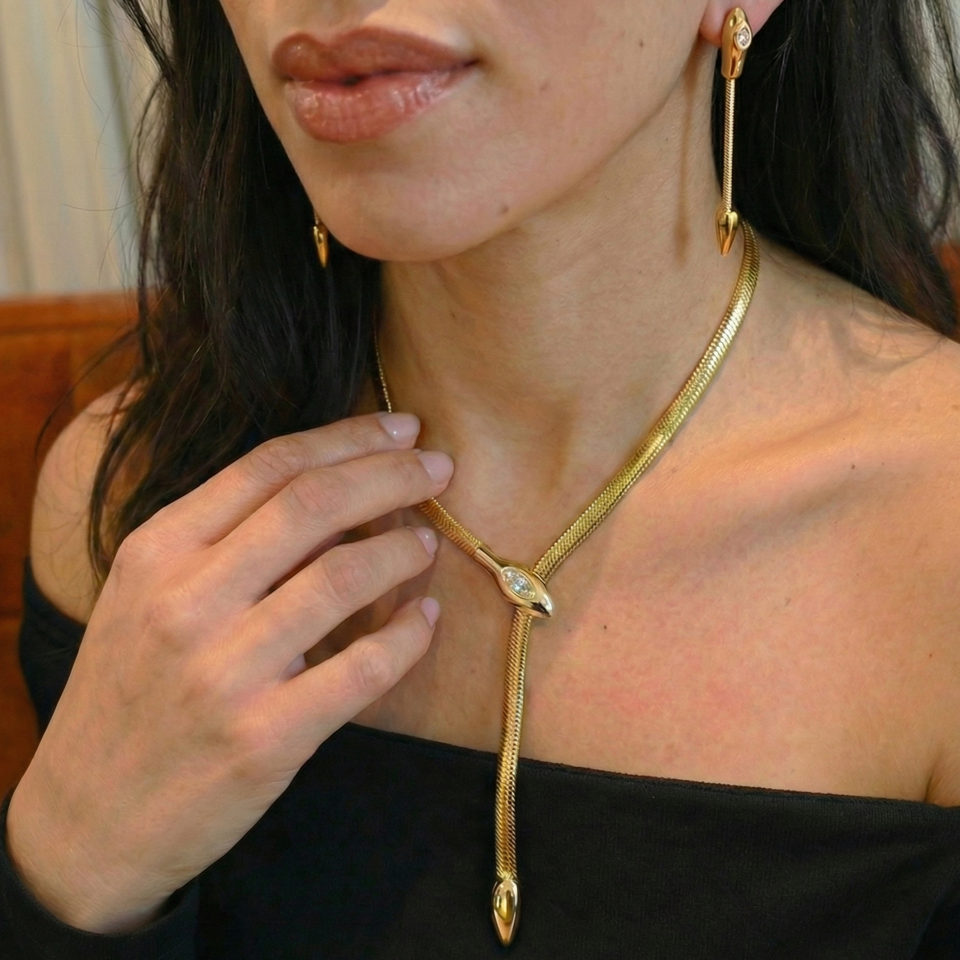 Woman wearing a gold snake necklaces and earrings against a neutral background