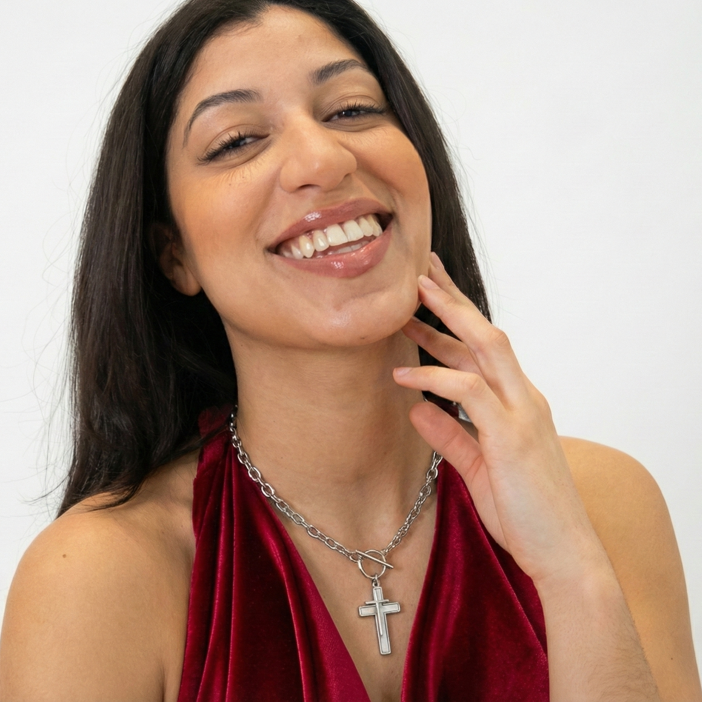 Woman wearing a red top and silver necklace with a cross pendant on a white background
