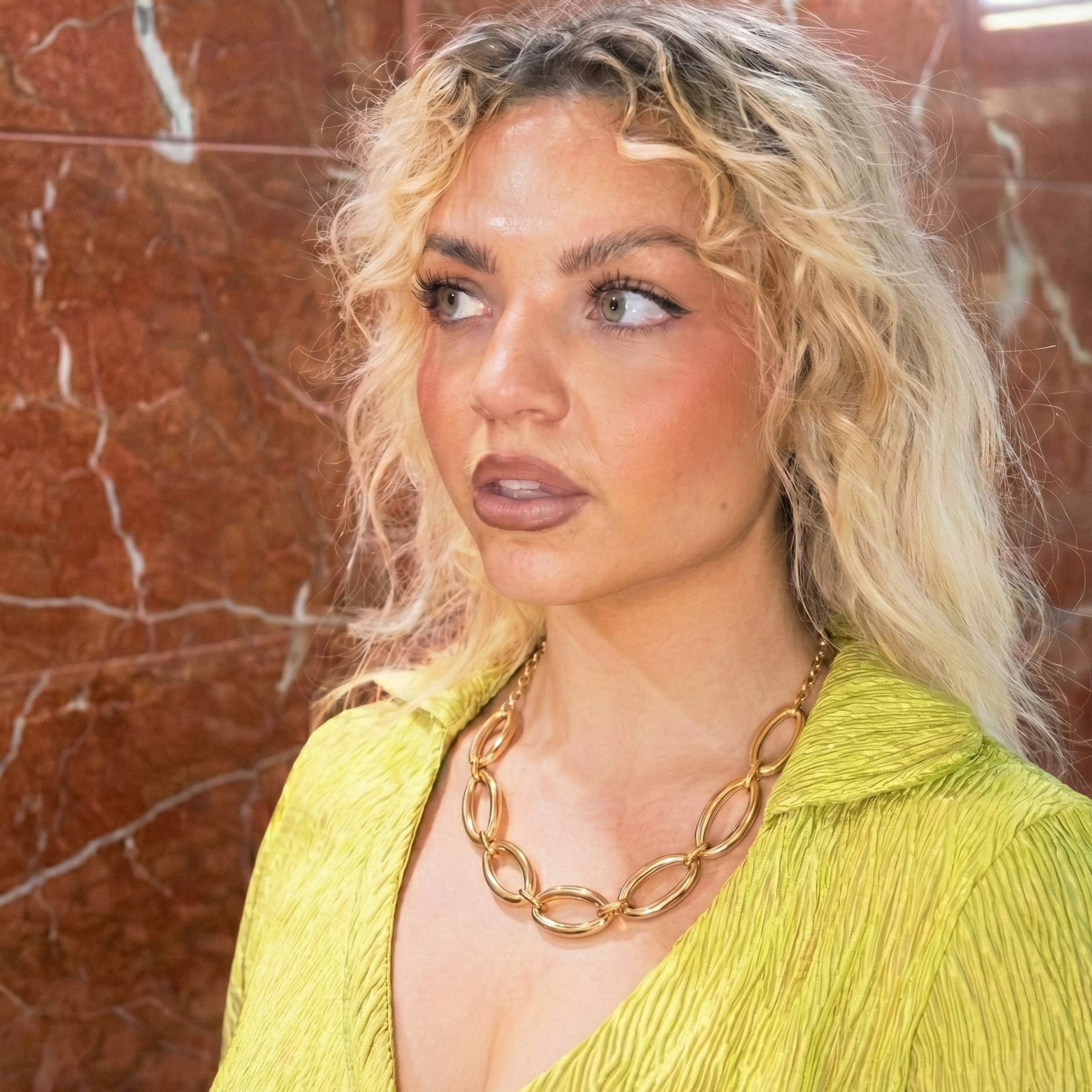 Woman wearing a yellow top and gold necklace against a brown marble wall