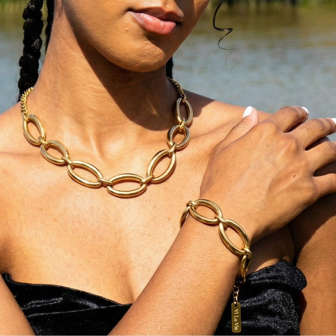 Woman with braided hair wearing gold jewelry by a body of water